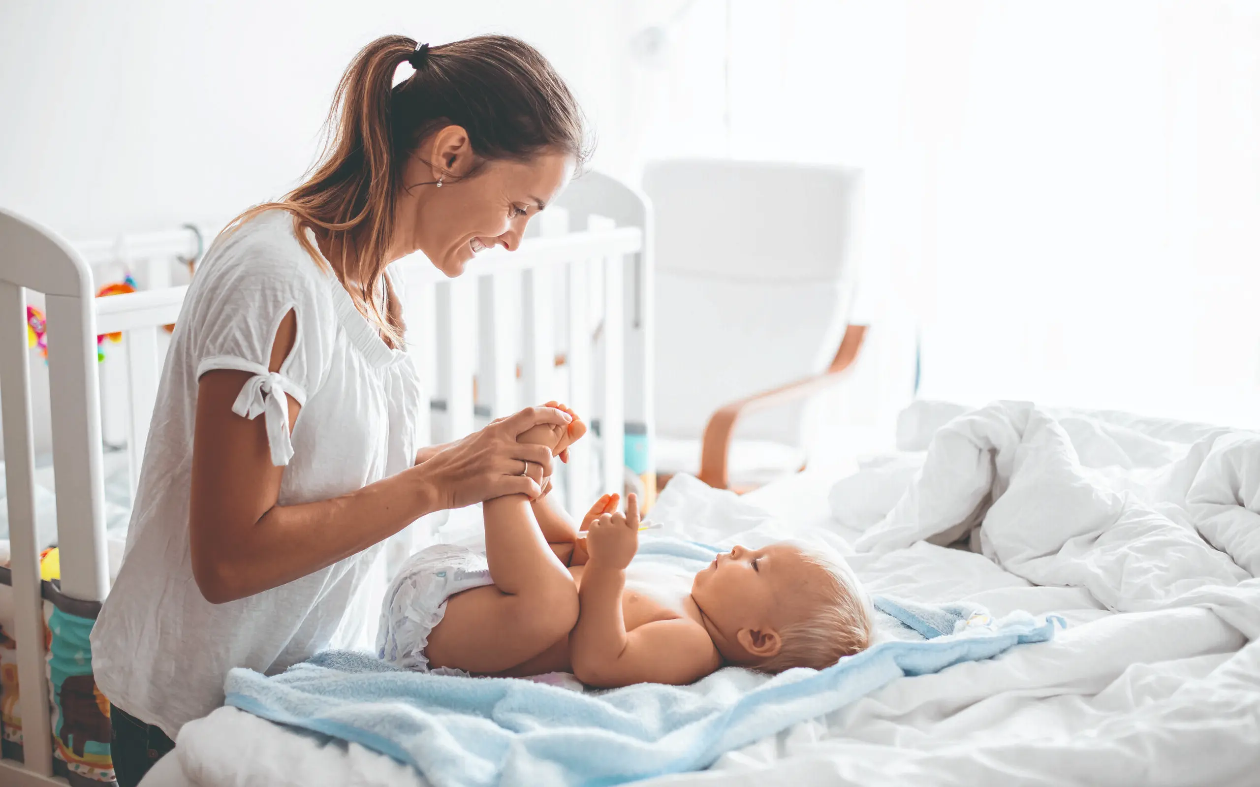 Young mom, changing baby diaper after bath in sunny bedroom